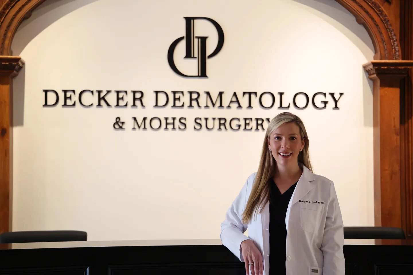 Woman in a white coat stands in front of a dermatology clinic sign.